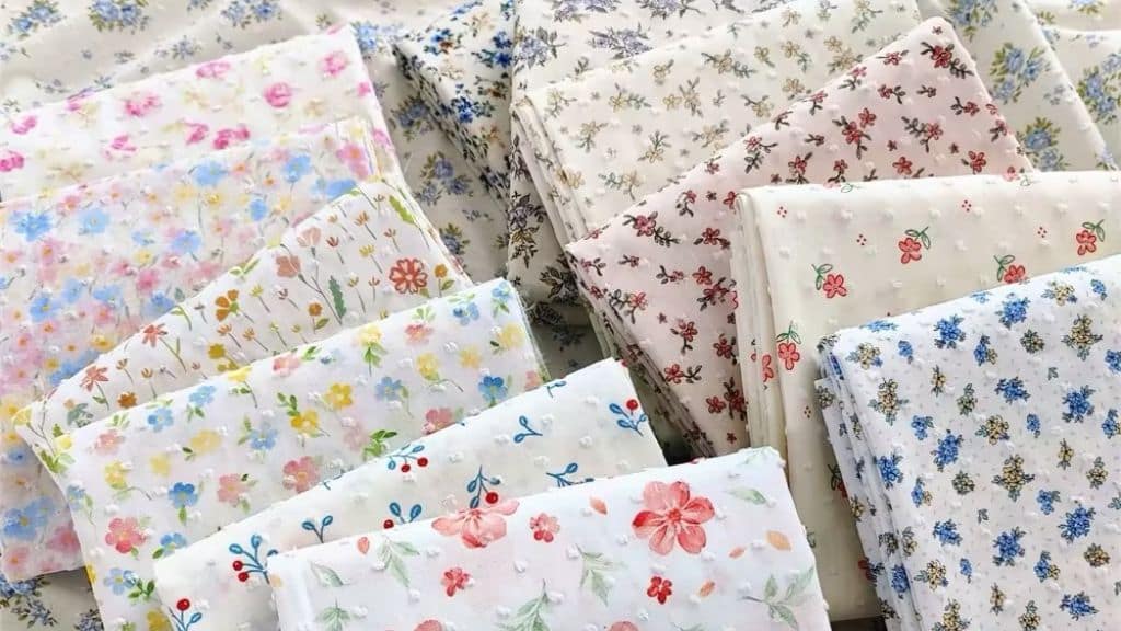 Assorted colorful floral printed dotted swiss fabrics stacked together.