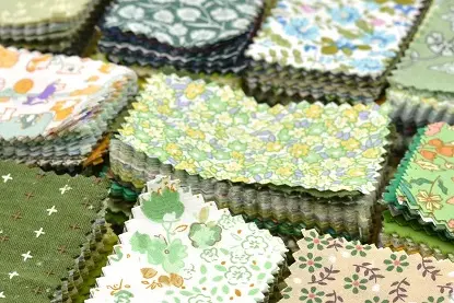 Several coordinated quilting cotton fabric bundles featuring patterns in yellow, green, and brown tones.