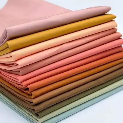 A stack of premium solid color cotton quilting fabrics in a sophisticated Morandi color palette, including muted pink, mustard, and sage green.